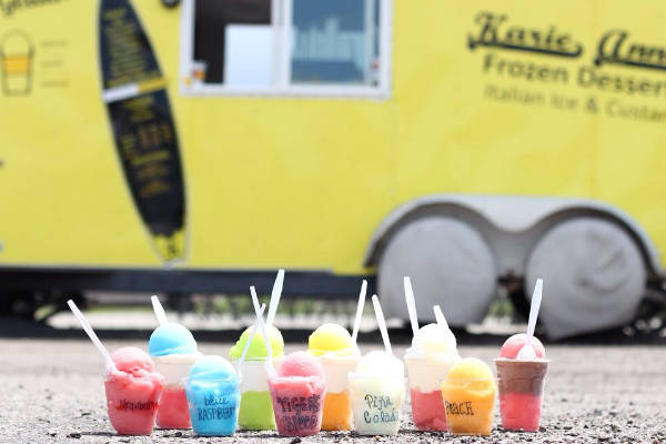 a selection of gelatis and italian ice resting on the ground in front of a dessert truck.